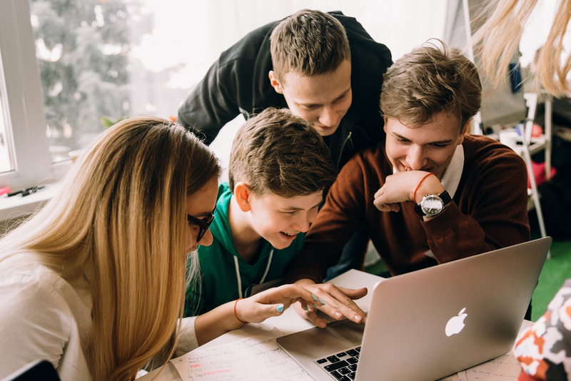 A group of four people happily collaborate while looking at a laptop.